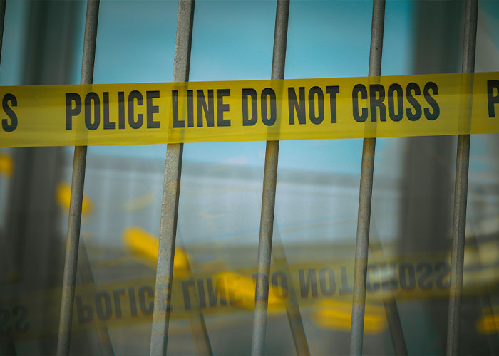 Police line tape behind metal bars at the scene of a tragic forklift accident involving a CEO and a fleeing worker.