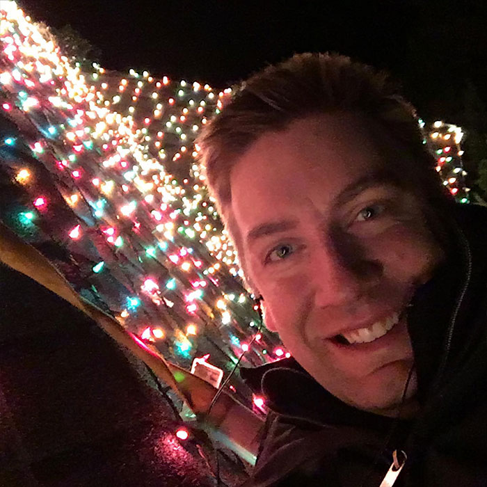 Man smiling next to a tree wrapped in colorful Christmas lights, symbolizing the Christmas lawyer victory over HOA.
