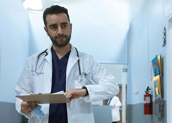 Male doctor with stethoscope and clipboard in hospital hallway, representing unprofessional things doctors said to patients.
