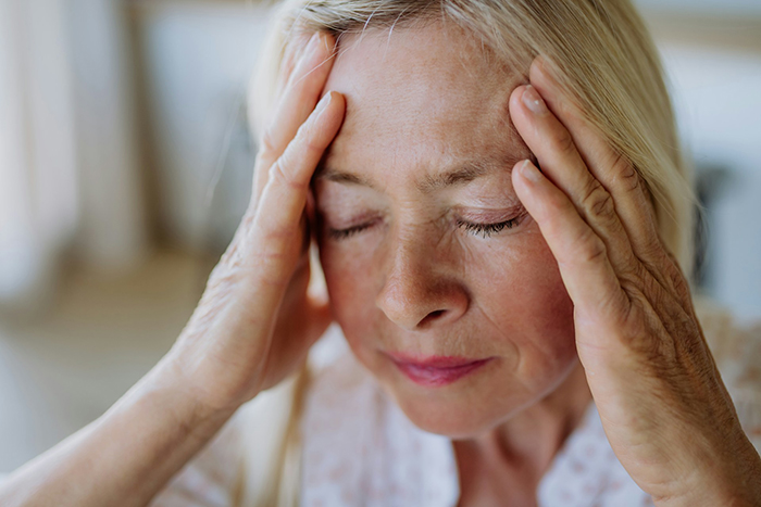Elderly woman holding her head in frustration, portraying stress related to MIL&rsquo;s plan to make bride look ugly in wedding illustration.