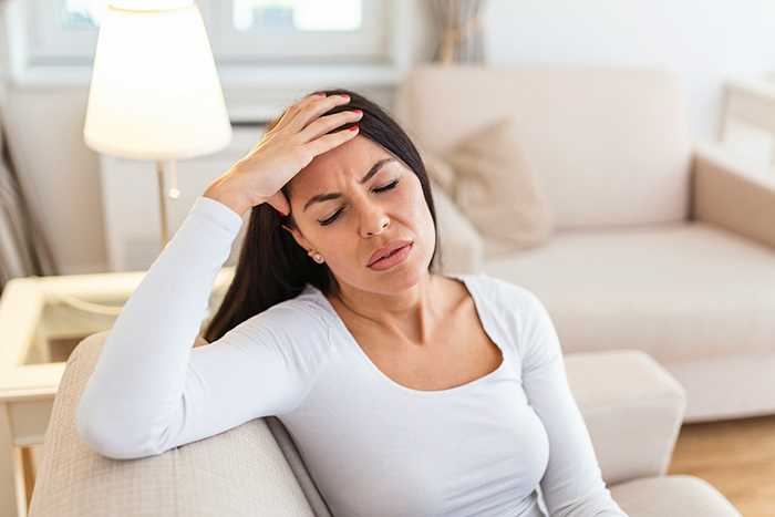Woman sitting on couch with hand on forehead, appearing stressed while babysitting a baby during Christmas time.