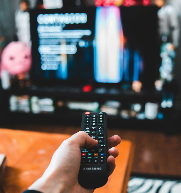 Hand holding Samsung remote control pointed at TV screen, symbolizing man shaming girlfriend for loving fiction. Hand holding Samsung remote control pointed at TV screen, symbolizing man shaming girlfriend for loving fiction.