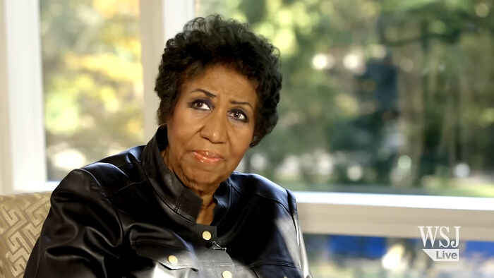 Elderly woman in black leather jacket sharing fascinating secrets about celebrities in an interview setting with natural light.