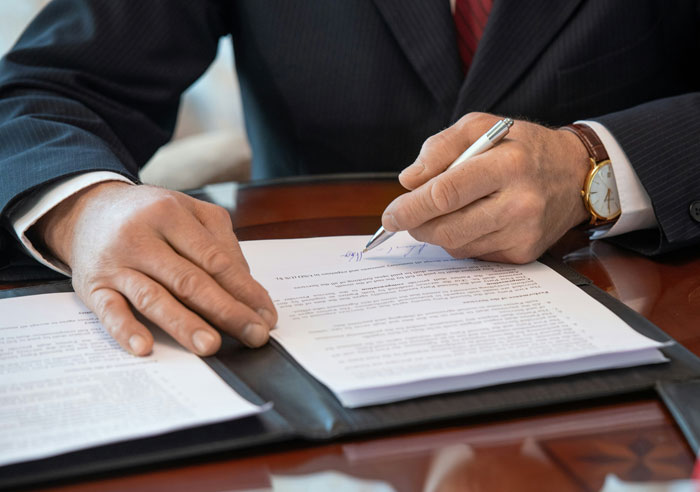 Man in a suit signing documents at a desk, representing office scandals that turned workplaces upside down.