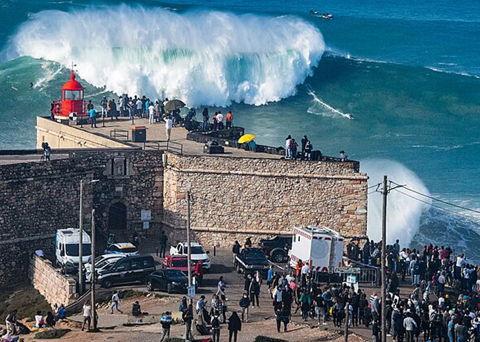 Huge ocean wave crashing near a crowded stone pier, one of the places from around the world that look AI generated but are real.
