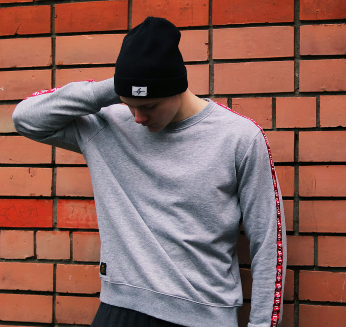 Teen boy wearing a black beanie and gray sweatshirt looking down against a brick wall, showing next-level evil vibe.