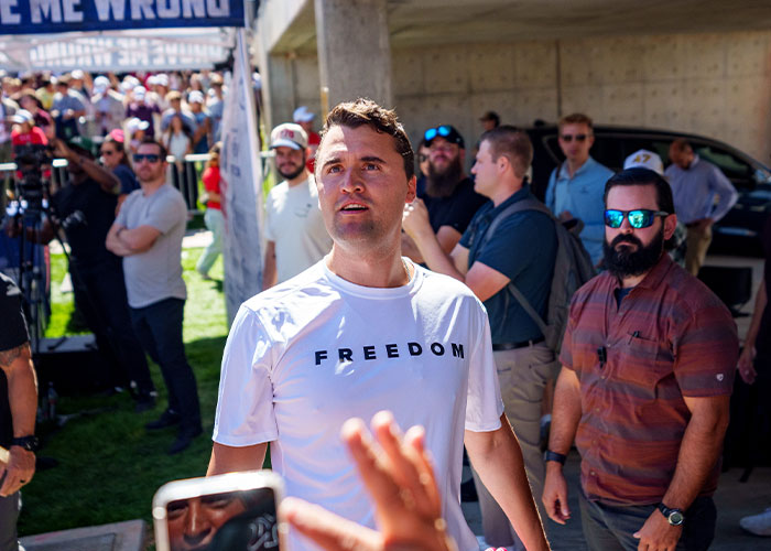Man wearing a white freedom shirt surrounded by people, representing Erika Kirk&rsquo;s curated moment with husband Charlie.