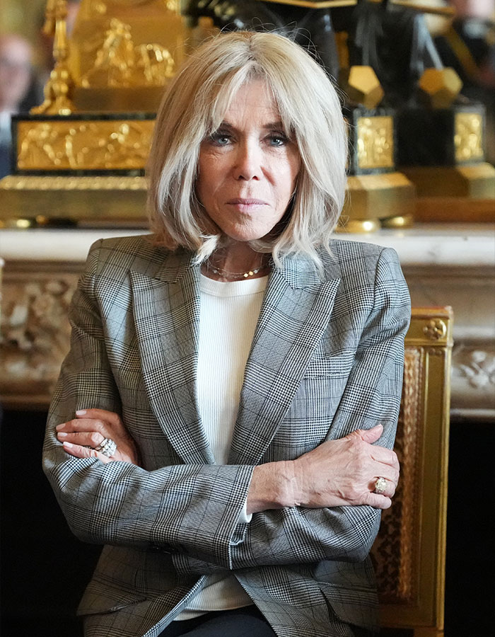 Brigitte Macron seated with arms crossed, wearing a plaid blazer in an ornate room, highlighting reaction to Candace Owens comment
