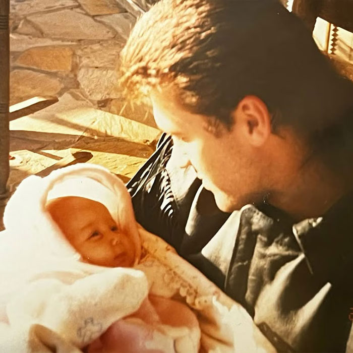 Man holding a newborn baby wrapped in a blanket, representing a woman claiming to be Miley Cyrus true birth mother.