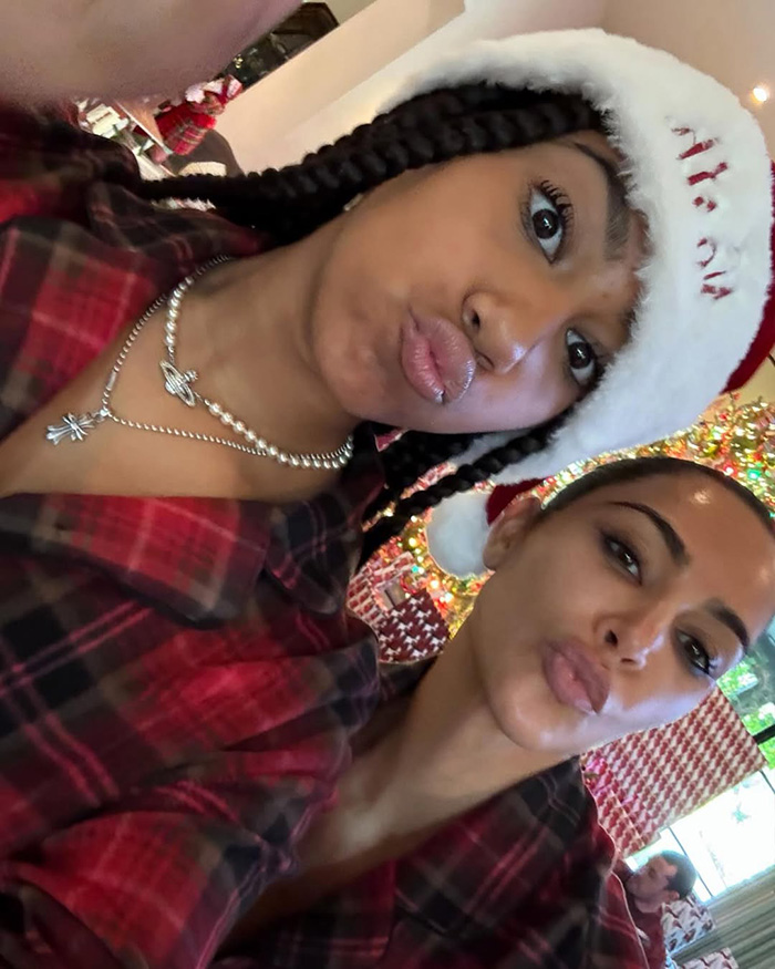 Two women wearing Santa hats and red plaid outfits, posing for a selfie related to Kim Kardashian Christmas card kids home life.