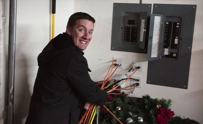 Man known as Christmas lawyer smiling while unplugging Christmas lights near electrical panel in basement room.