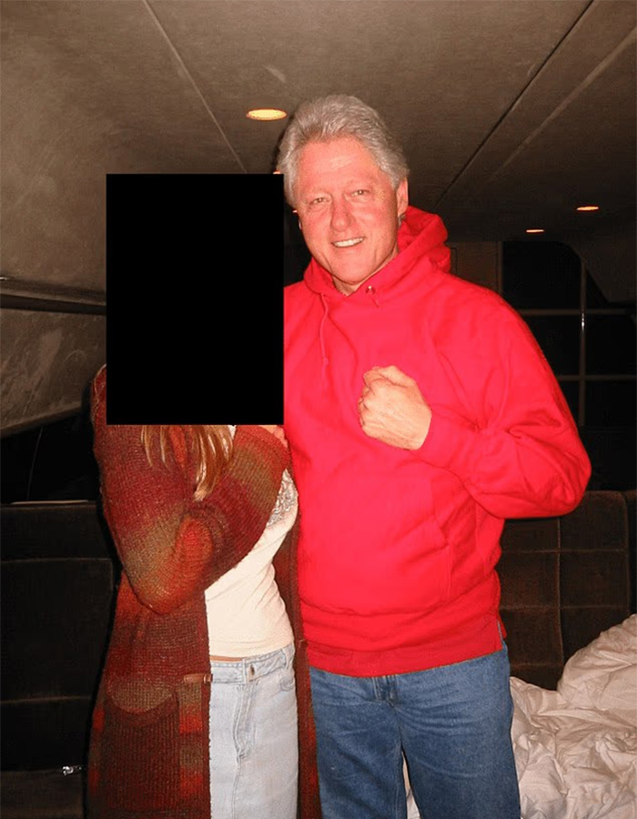 Man in red hoodie smiling beside a person with obscured face inside a dimly lit room, toddler's foot reportedly visible in photo.