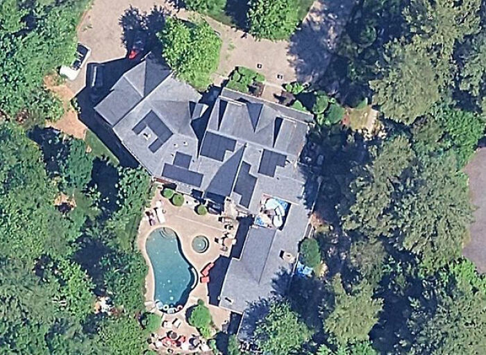 Aerial view of a family's multi-million dollar mansion with pool surrounded by trees in a lush green area.
