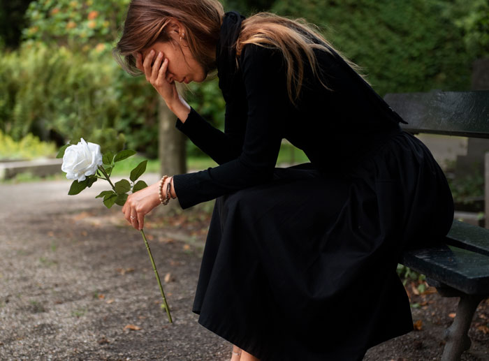 Woman in black dress sitting on a bench holding a white rose, reflecting on the toughest things couples chose to forgive.