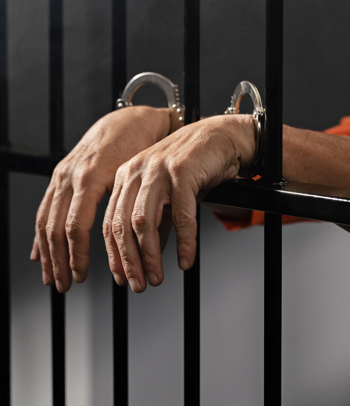 Hands in handcuffs gripping jail bars, illustrating people terrified of next-level evil kids behind bars.