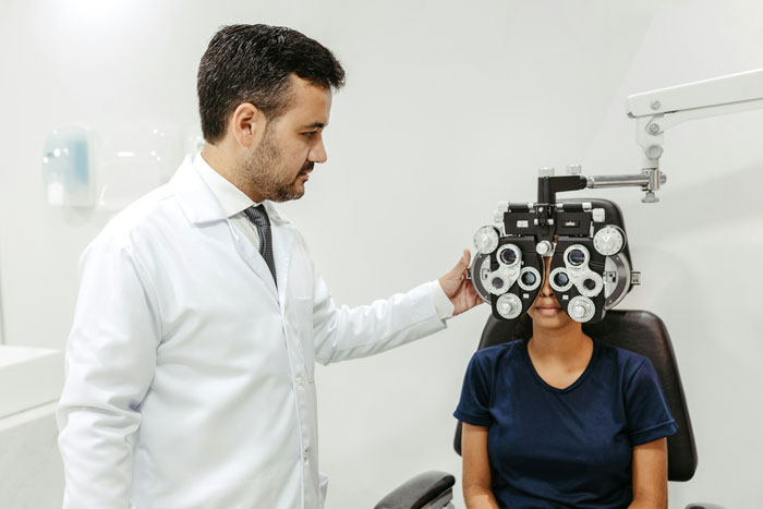 Doctor adjusting eye exam equipment while patient undergoes vision test in a clinical setting during an eye exam.