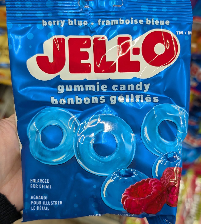 Blue Jell-O gummie candy bag held in hand, showcasing berry blue flavor with vibrant packaging in a store aisle.