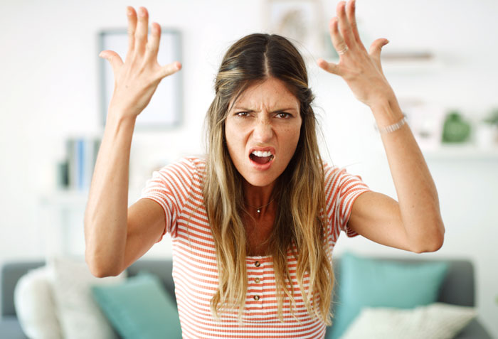 Angry woman in striped shirt raising hands, expressing frustration about family rehoming or renaming 11-year-old cat. Angry woman in striped shirt raising hands, expressing frustration about family rehoming or renaming 11-year-old cat.