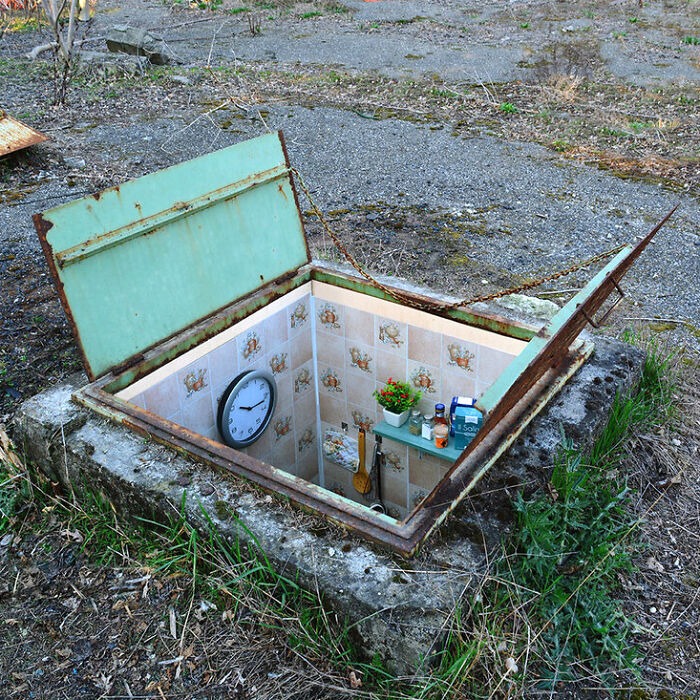 Rusty green hatch opens to reveal a trippy picture of a tiled underground room with clock and plants inside.