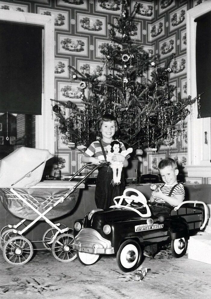 Two children with vintage toys near a decorated Christmas tree in a powerful old photo capturing everyday life.