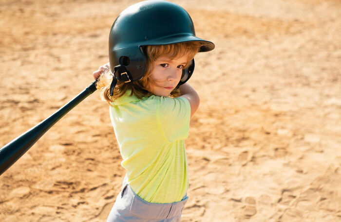 Young child in a batting helmet holding a baseball bat, illustrating crazy things people have done to make their ex pine.