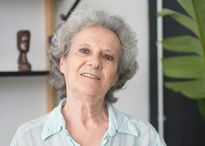 Older woman with gray hair and light blue blouse indoors, illustrating shocked reactions to unhinged things their MIL said.