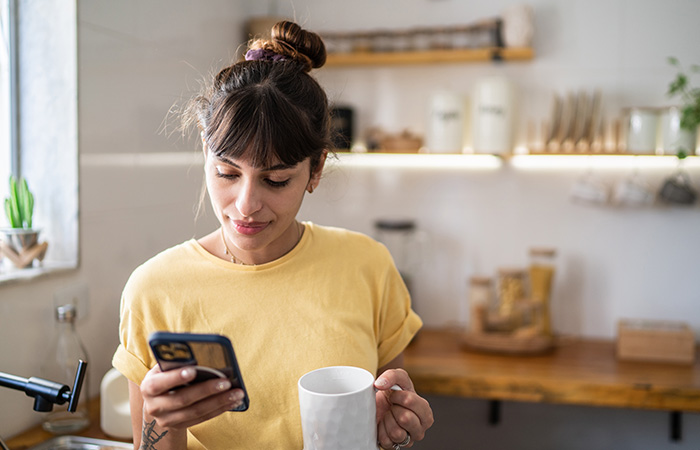 Young woman holding a mug and looking at her phone, representing traits men find attractive in women naturally.