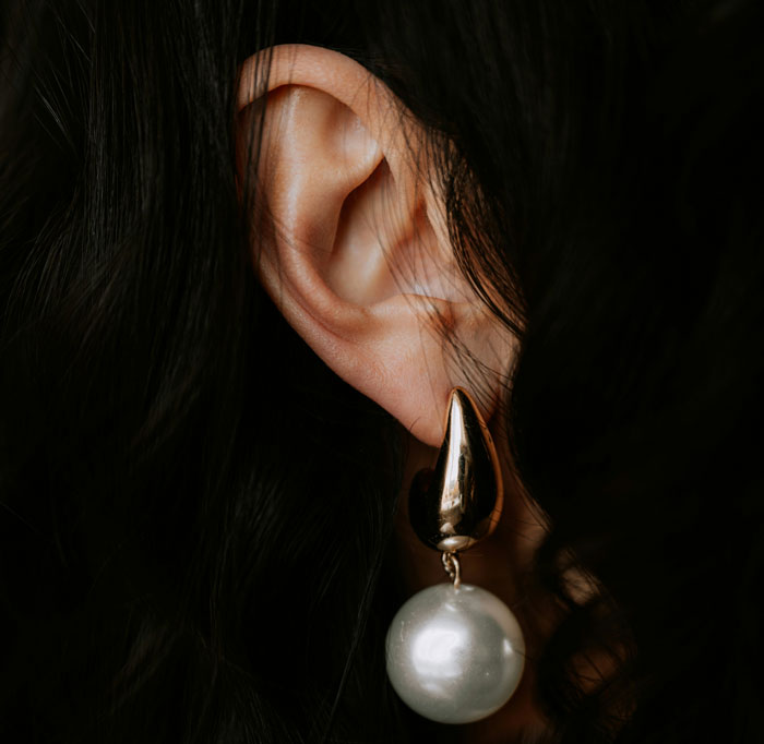 Close-up of an ear with a gold and pearl earring, illustrating embarrassing moments shared in front of doctors.