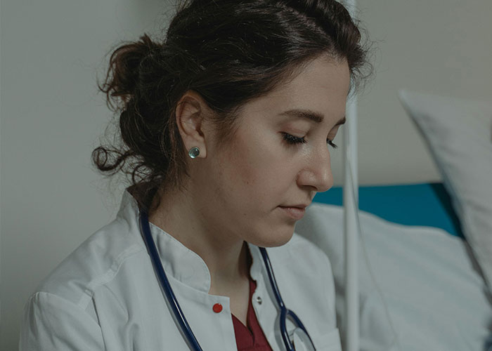 Female doctor in a white coat and stethoscope looking down thoughtfully in a medical setting about unprofessional doctor comments.