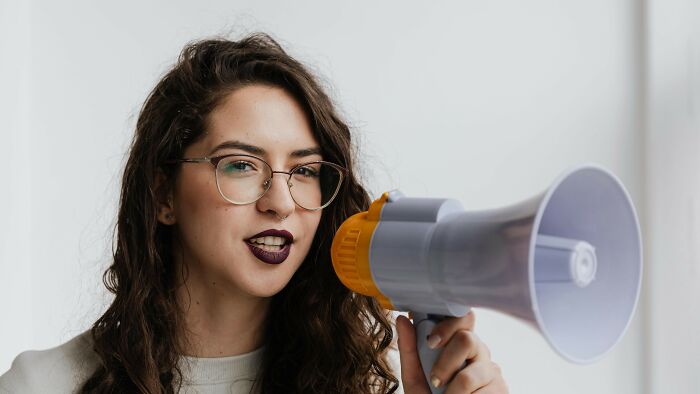 Young woman with glasses using a megaphone to cast her vote in ambiguous fault and right situations discussion