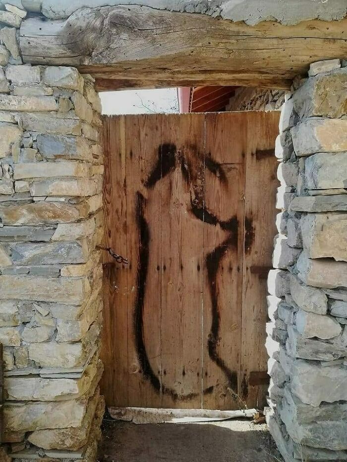 Rustic wooden gate with faded graffiti in a stone wall, capturing nostalgic Eastern Europe humor and memories.