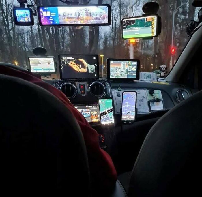 Car dashboard filled with multiple GPS devices and screens showing maps and navigation in an Eastern Europe setting.