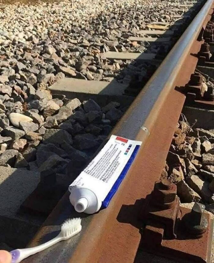 Tube of toothpaste and toothbrush placed on rusty train tracks, a funny meme relatable to growing up in Eastern Europe.