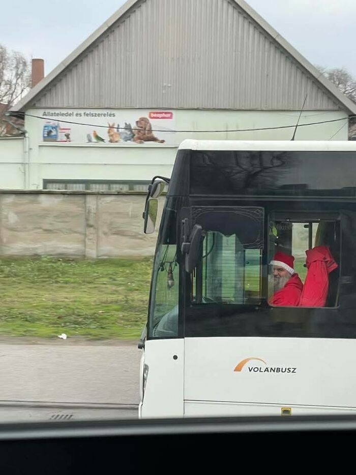 Man dressed as Santa Claus sitting in a bus driver seat of a white Volánbusz in Eastern Europe setting.