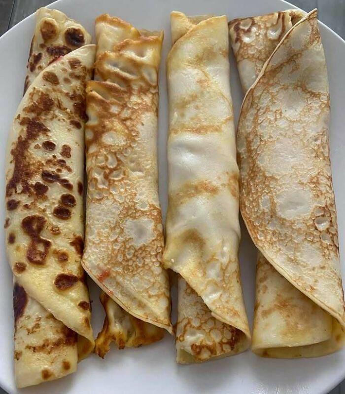 Four rolled Eastern European crepes on a white plate, showcasing traditional homemade comfort food.