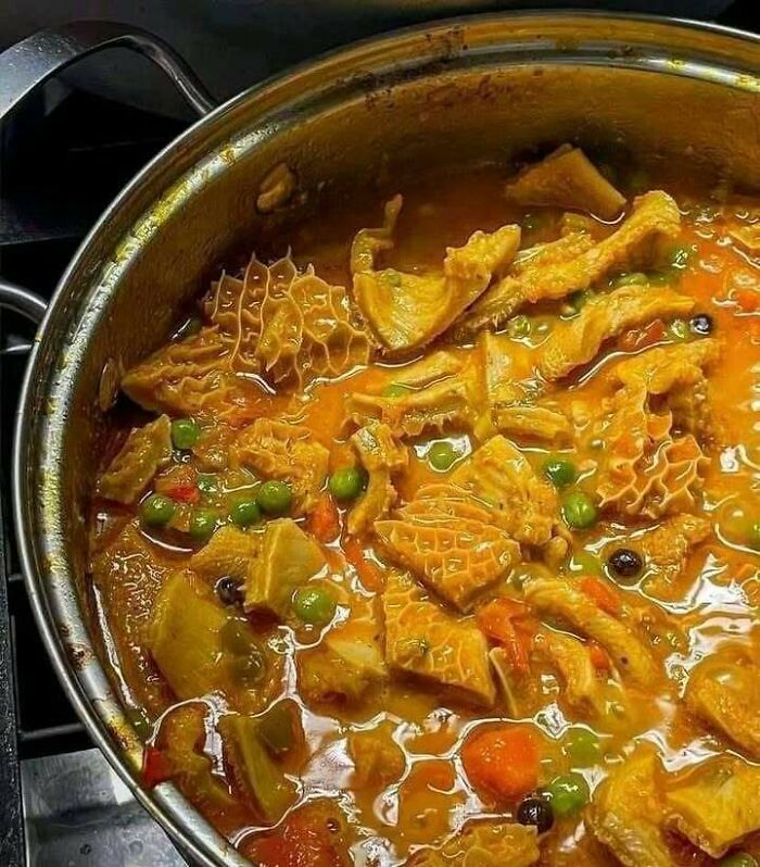 Traditional Eastern European tripe stew cooking in a pot with vegetables, peas, and rich spicy broth.