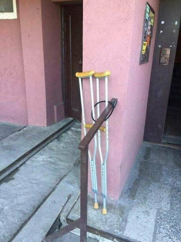 Pair of yellow-handled crutches leaning against a pink wall next to a rusty metal railing in Eastern Europe setting.
