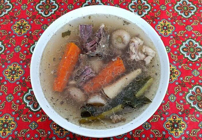 Traditional Eastern European soup with meat, carrots, and vegetables served in a white bowl on patterned fabric