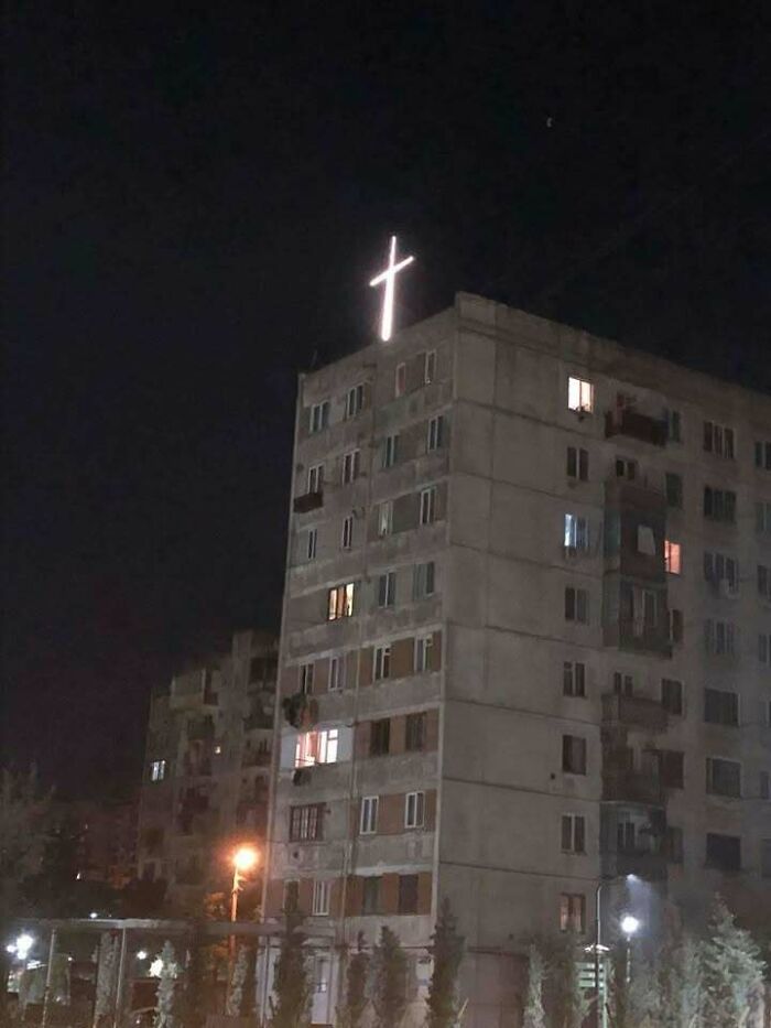 Apartment building at night with a glowing cross on the roof, showcasing Eastern Europe humor and culture in a meme style.