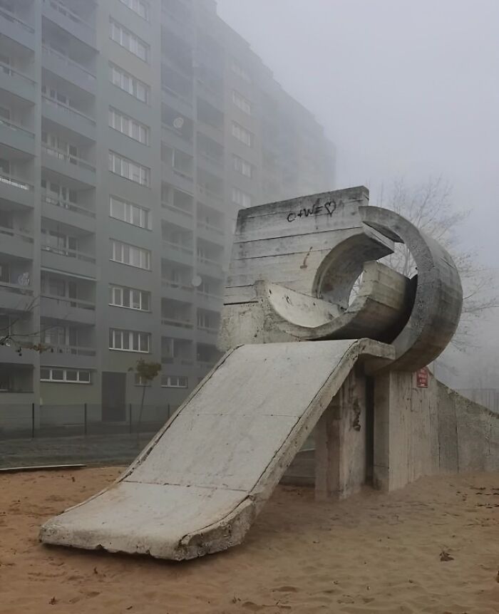 Concrete playground slide with brutalist architecture in a foggy Eastern European residential area, reflecting childhood nostalgia.