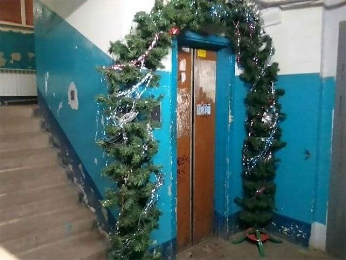 Elevator decorated with mismatched Christmas garland in a worn Eastern European apartment building hallway.