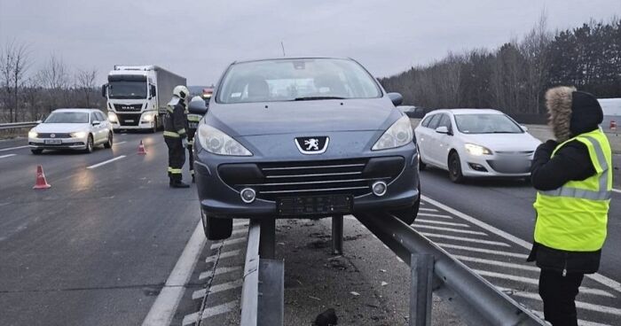 Car stuck on highway guardrail with emergency responders and traffic on a cloudy Eastern Europe road scene