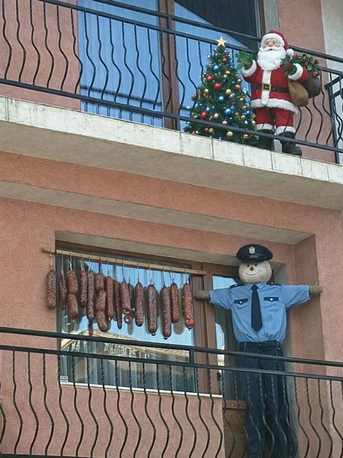 Balcony scene with sausages hanging to dry, a scarecrow dressed as a policeman, and holiday decorations in Eastern Europe.