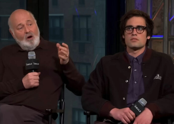 Two men holding microphones during an interview, discussing the horrific state of Nick Reiner's hotel room.