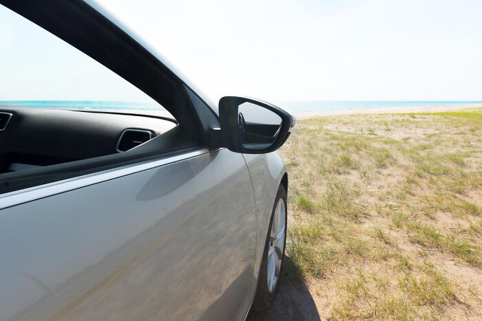 Silver car parked near a beach with ocean view, evoking unresolved mysteries people carry with them on journeys.
