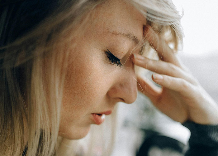 Close-up of a distressed woman touching her forehead, reflecting on insane things her ex ever did in wild stories shared by people.
