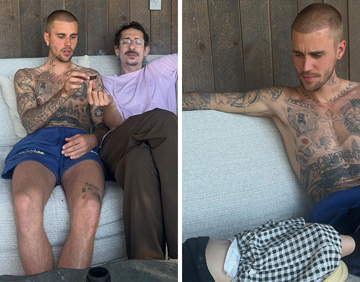 Two men sitting on a couch, one shirtless with tattoos, relaxed setting reflecting major celebrity scandals in 2025.