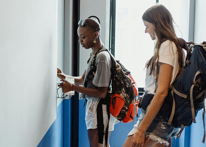 Two young people with backpacks using a wall-mounted device, illustrating luxury industries and rip-offs insight.