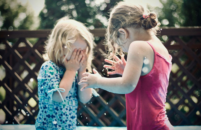 Two kids playing in water with one covering face, capturing next-level evil behavior of kids people fear.