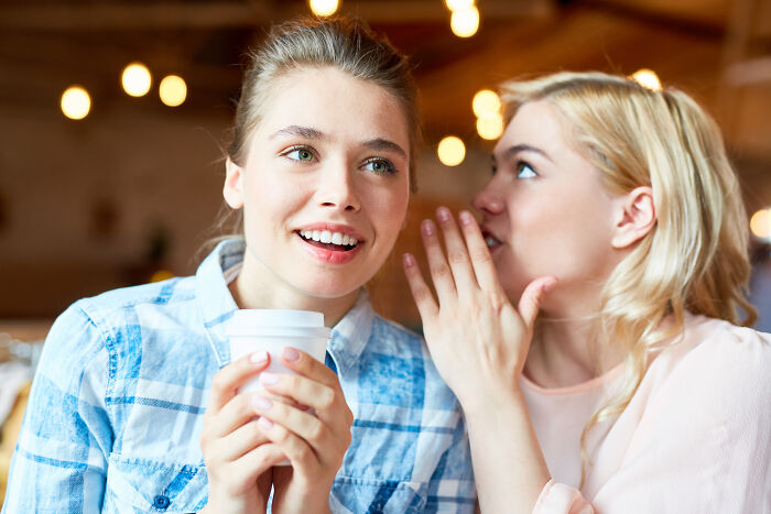Two young women sharing a secret while enjoying coffee, illustrating small tricks that make being a grown-up easier.